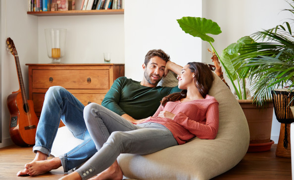 Aufnahme eines lächelnden jungen Paares, das sich zu Hause auf einem Sitzsack entspannt und miteinander unterhält | Der Dämmstoff | Foto von kupicoo - istockphoto.com