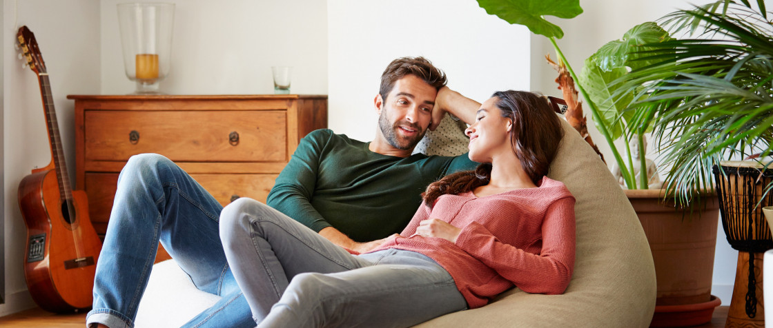 Aufnahme eines lächelnden jungen Paares, das sich zu Hause auf einem Sitzsack entspannt und miteinander unterhält | Der Dämmstoff | Foto von kupicoo - istockphoto.com